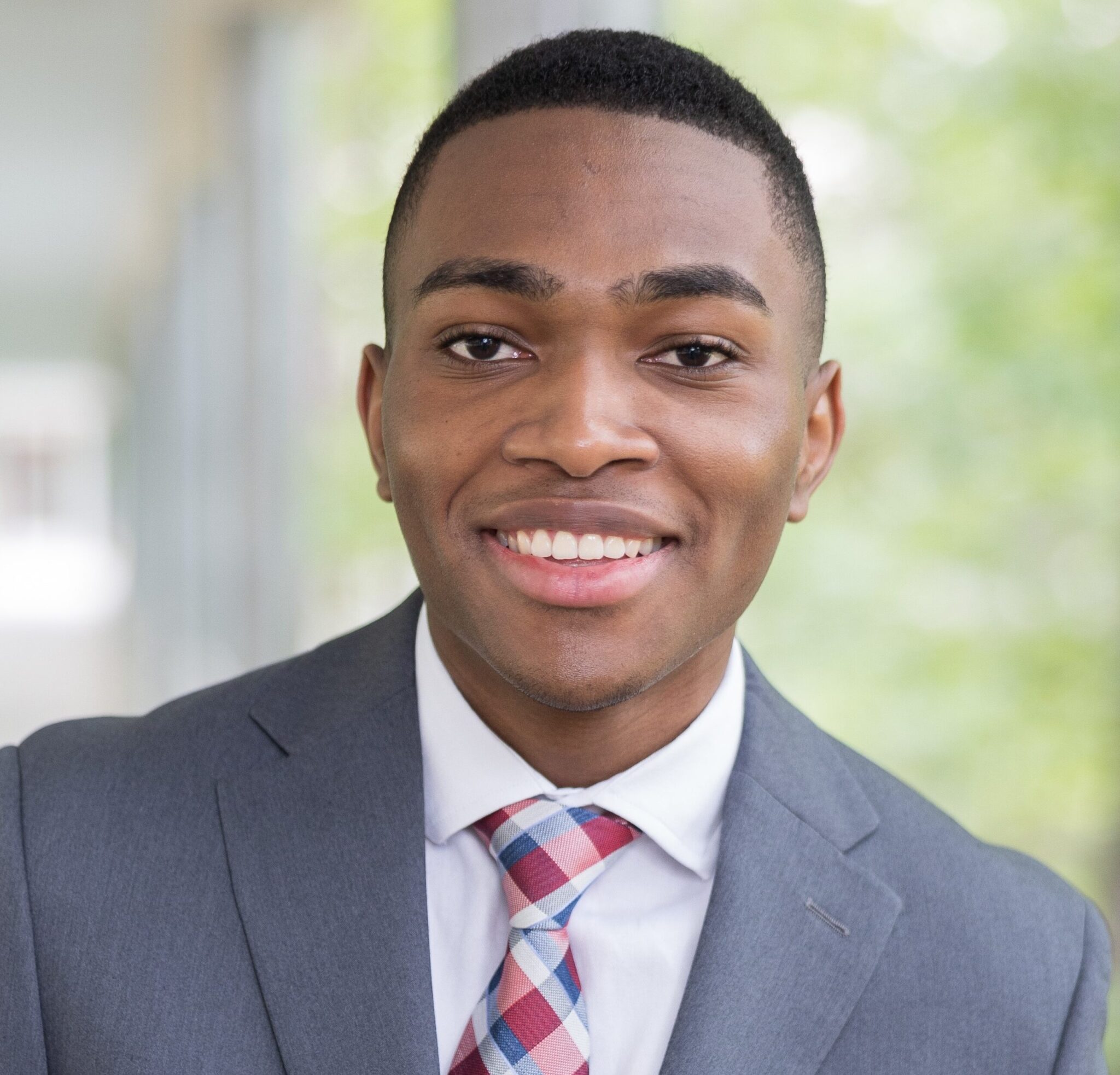 Photo of Evon Thompson, a Black person with short hair wearing a suit and tie and smiling at the camera