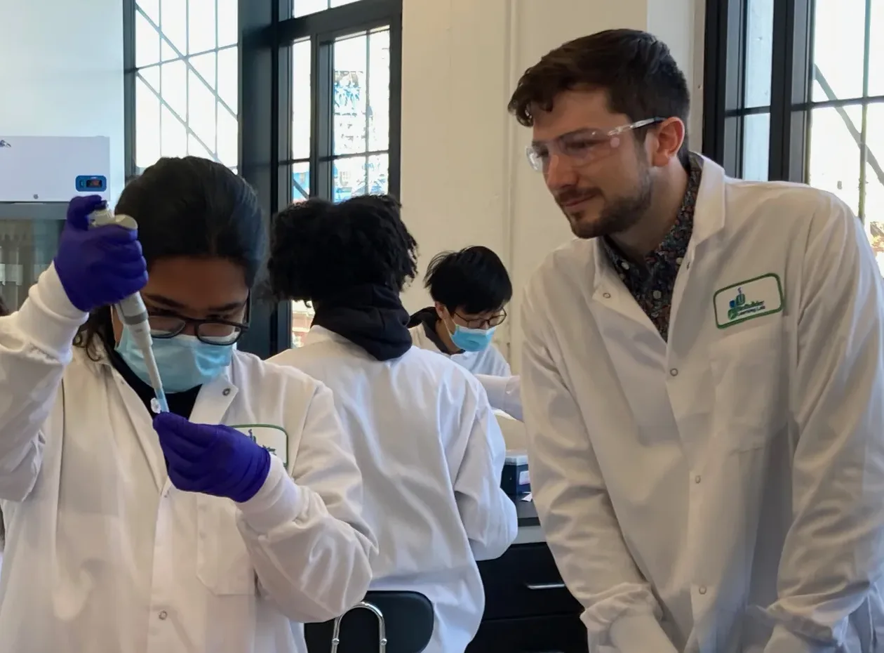 A person in a BioBuilder lab coat mentoring students